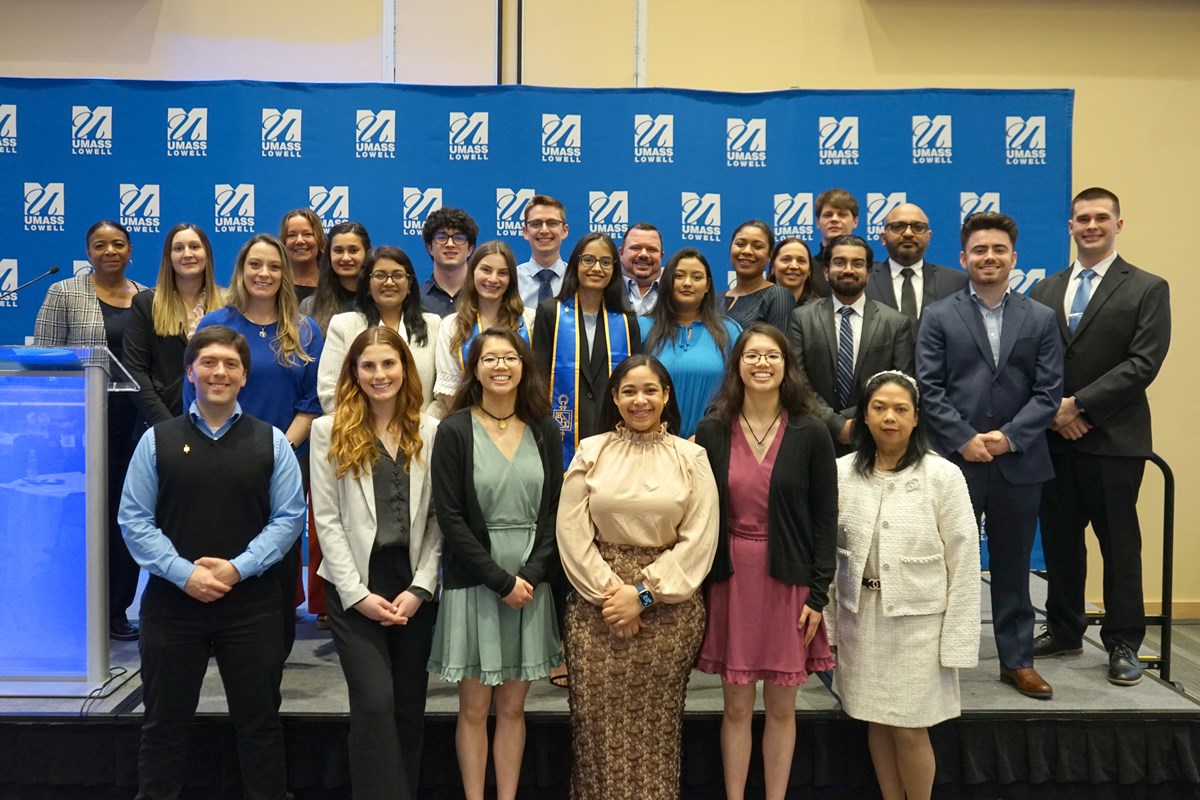 27 people pose for a group photo while standing in front of a blue backdrop.